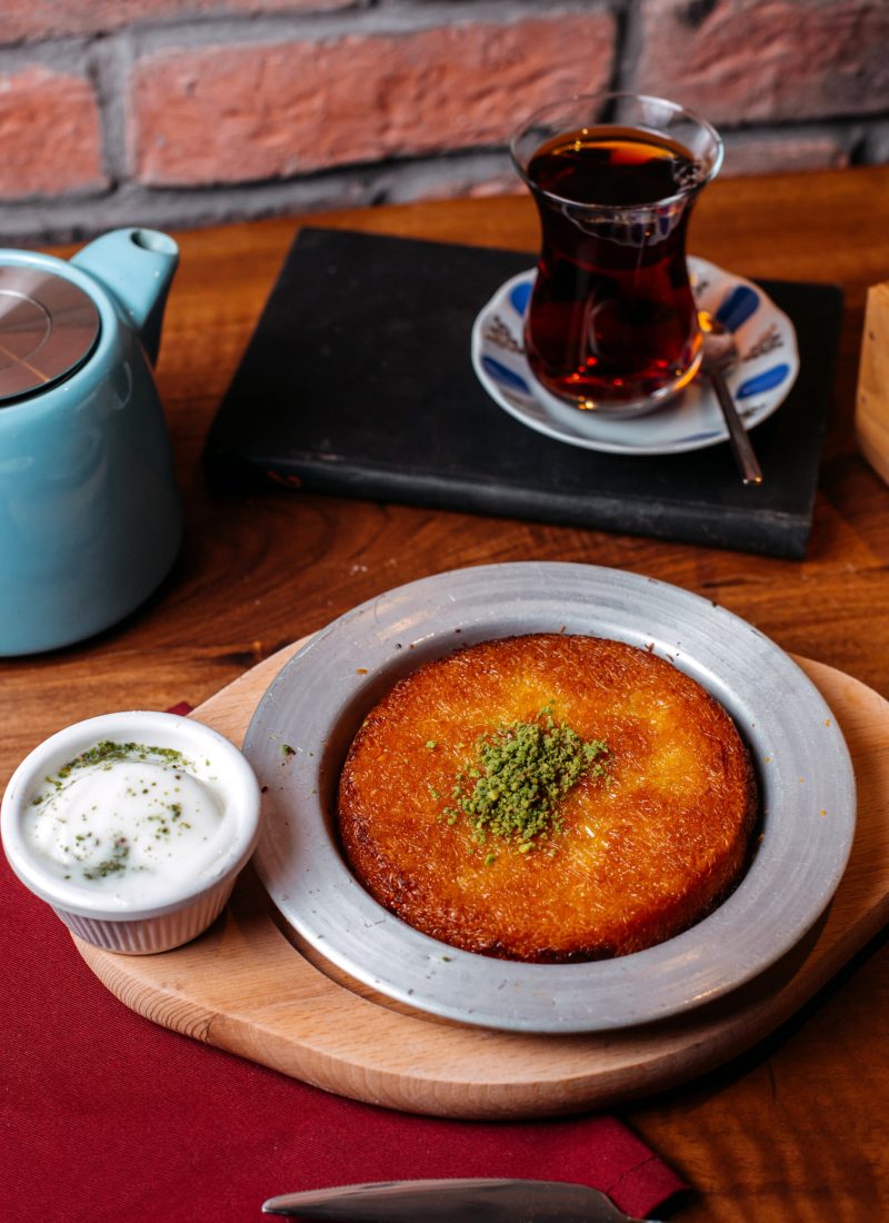 side view of traditional turkish dessert kunefe with pistachio powder and cheese on a wooden table