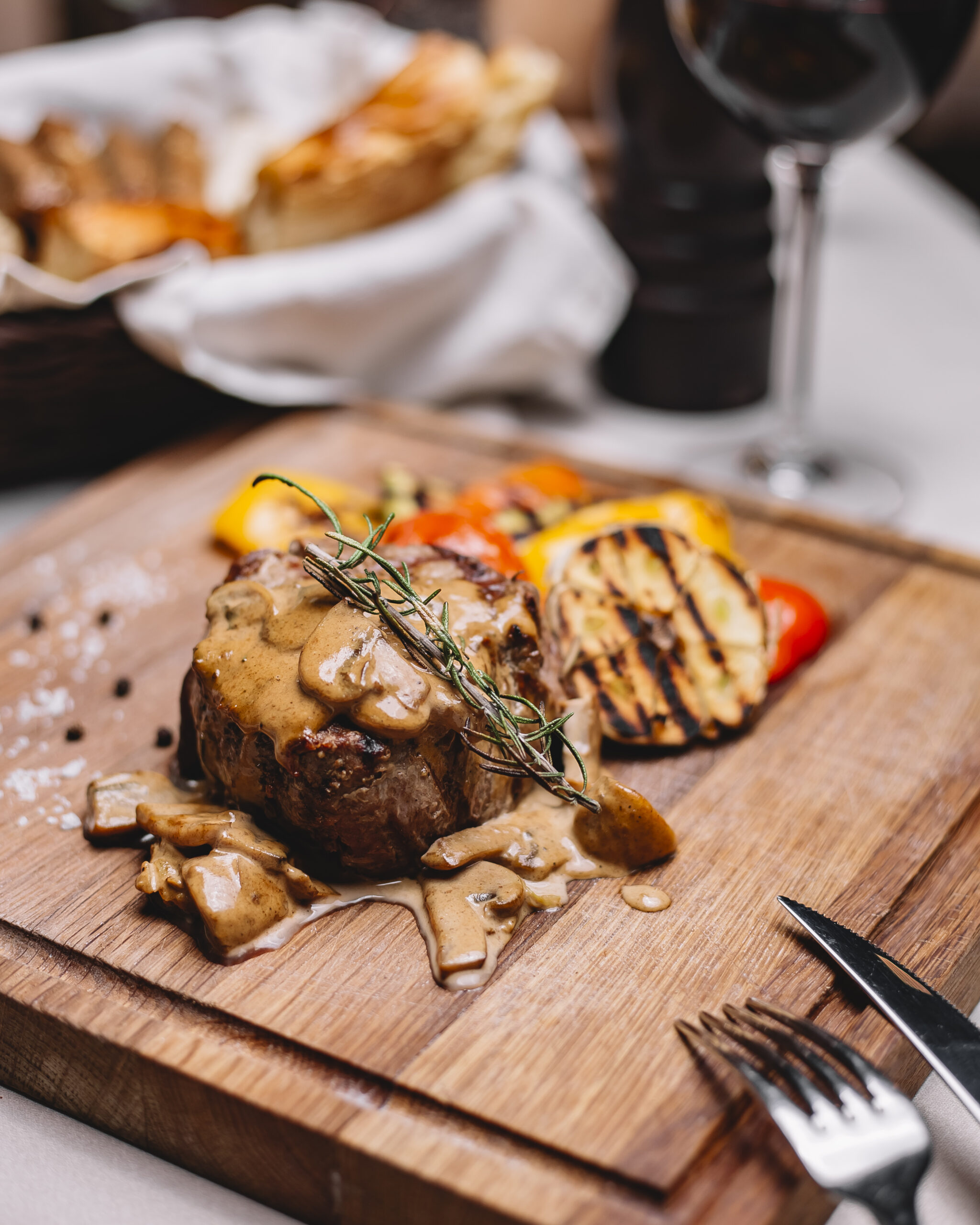 side view of grilled meat medalion with sauce and grilled vegetables on a wooden board